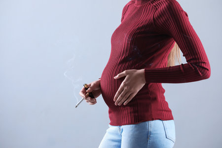 Young pregnant woman smoking cigarette on gray background, closeup. Space for textの写真素材