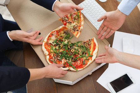 Office employees having pizza for lunch at the workplace, closeup. food deliveryの写真素材