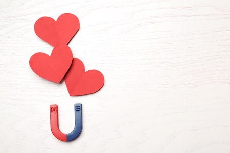 Magnet attracting red hearts on wooden background, top view with space for text. love conceptの写真素材