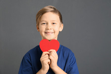 Cute boy with paper heart on gray background. Space for textの写真素材