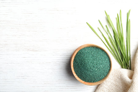 Bowl of spirulina powder, grass and napkin on white background, flat lay. Space for textの写真素材