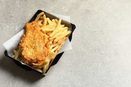 Disposable container with British Traditional Fish and potato chips on gray background. Space for...