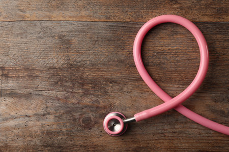 Pink stethoscope folded like awareness ribbon on wooden background, top view with space for text. breast cancer conceptの写真素材