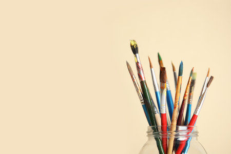 Glass with paint brushes on color background. Space for textの写真素材