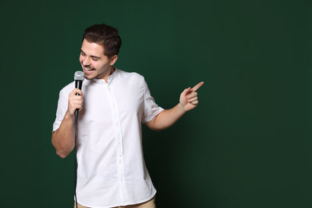 Young handsome man in casual clothes singing with microphone on color background. Space for textの写真素材