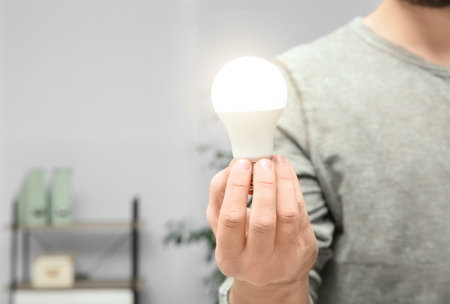 Man holding lamp bulb on blurred background, closeup with space for textの写真素材