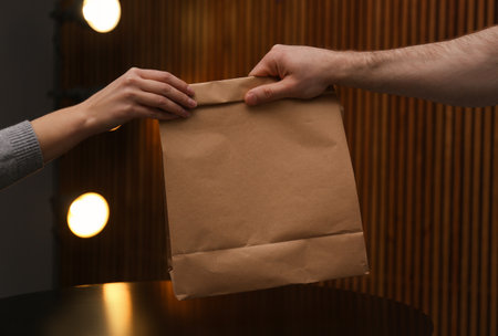 Man giving paper bag with order to customer in cafe, closeup. Mock up design