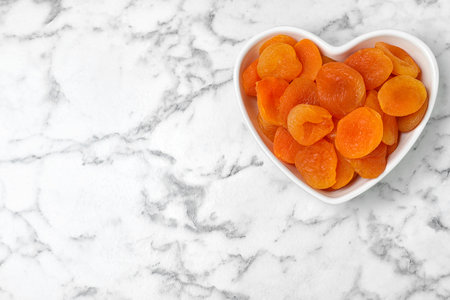 Heart shaped bowl of apricots on marble background, top view with space for text. Dried fruit as healthy foodの写真素材