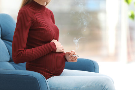 Young pregnant woman smoking cigarette at home, closeup. Harm to unborn babyの写真素材