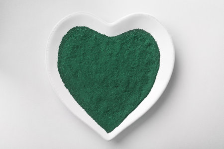 Heart shaped plate with spirulina algae powder on white background, top viewの写真素材