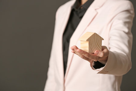 Female agent holding wooden house on dark background, closeup. home insuranceの写真素材