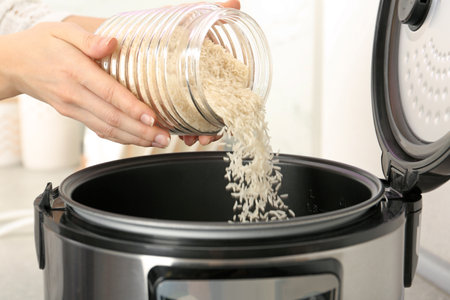 Woman pouring rice from jar into cooker in kitchen, closeupの写真素材