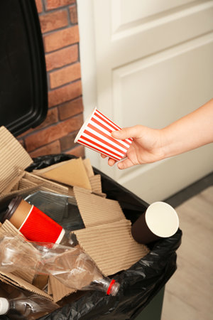 Young woman throwing popcorn cup in trash bin indoors, closeup. Waste recyclingの写真素材