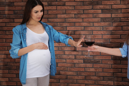 Future mother refusing glass of wine against brick wall. Alcohol abuse during pregnancyの写真素材