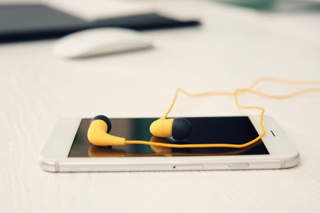 Smartphone with headphones on white table. Space for textの写真素材