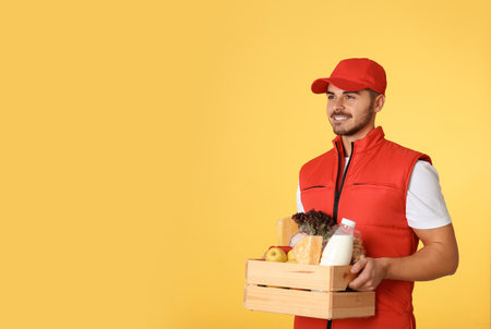 Food delivery courier holding wooden crate with products on color background. Space for textの写真素材