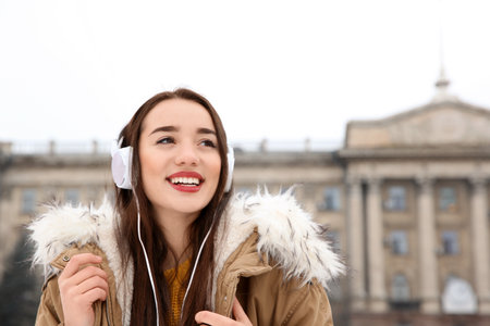 Beautiful young woman listening to music with headphones outdoors. Space for textの写真素材