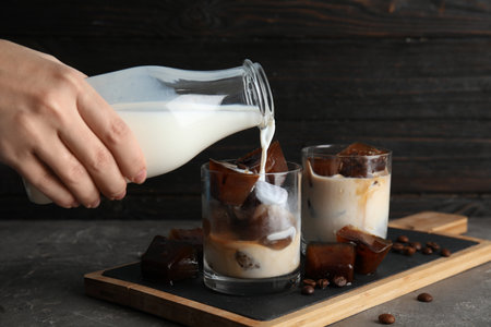 Woman pouring milk into glass with coffee ice cubes on tableの写真素材