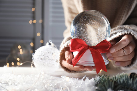 Woman holding Christmas snow globe with red bow on blurred background, closeup. Space for textの写真素材