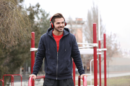 Young man with headphones listening to music and exercising on sports ground