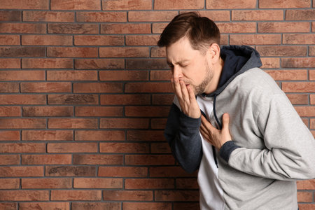 Man suffering from cough near brick wall. Space for text