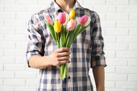 Man holding bouquet of beautiful spring tulips near brick wall, closeup. International Women's Dayの写真素材