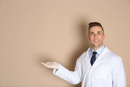 Male dentist holding something on color background. Space for textの写真素材