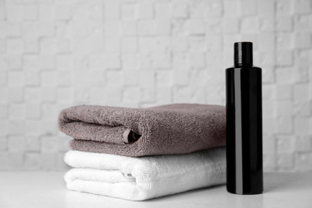 Folded towels and shampoo on table against white wallの写真素材