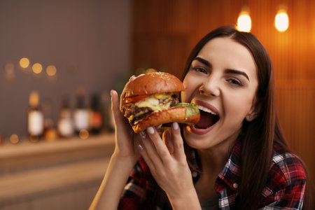 Young woman eating tasty burger in cafeの写真素材