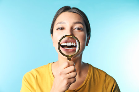 Young woman with healthy teeth and magnifier on color backgroundの写真素材