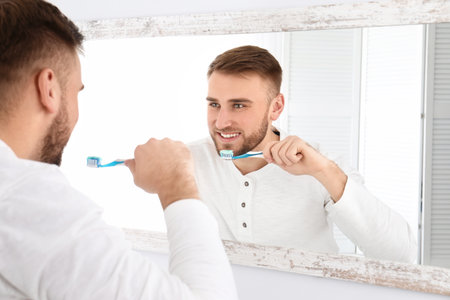 Young man cleaning teeth against mirror in bathroom