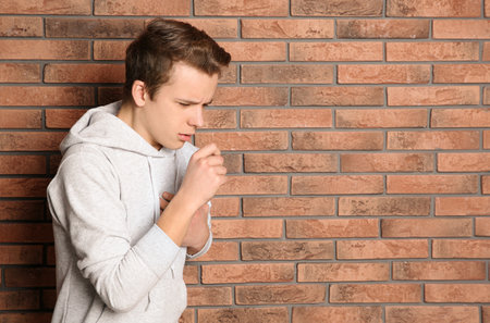 Teenage boy suffering from cough near brick wall. Space for textの写真素材