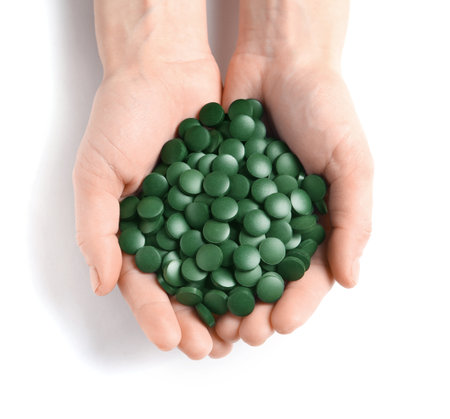 Woman holding heap of green spirulina pills on white background, top viewの写真素材