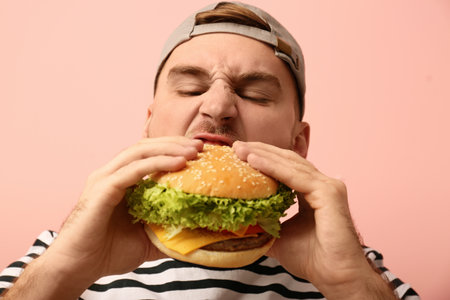Young man eating tasty burger on color backgroundの写真素材
