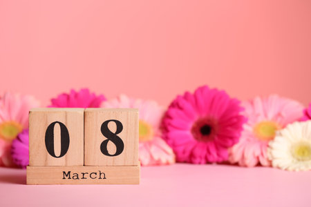 Wooden block calendar and flowers on table against color background, space for text. International...