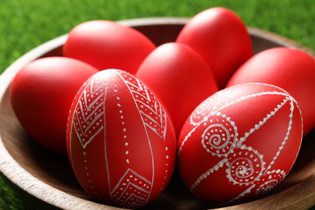Wooden bowl with red painted Easter eggs on green grass, closeupの写真素材
