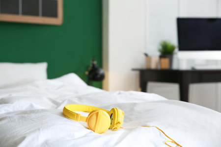 Stylish modern headphones with earmuffs on bed against blurred background, space for textの写真素材