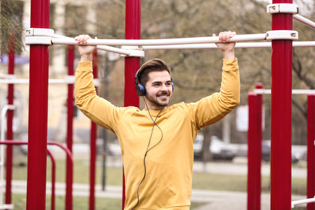 Young man with headphones listening to music and exercising on sports ground