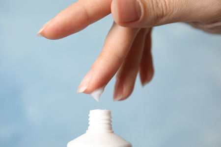 Woman applying hand cream on color background, closeup
