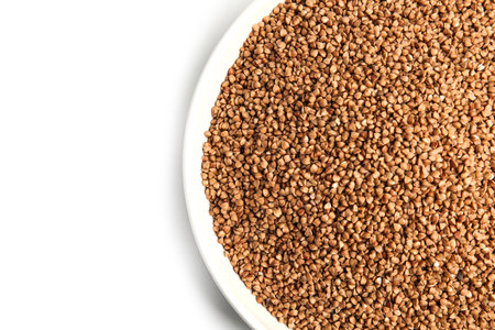 Bowl with uncooked buckwheat on white background, top view