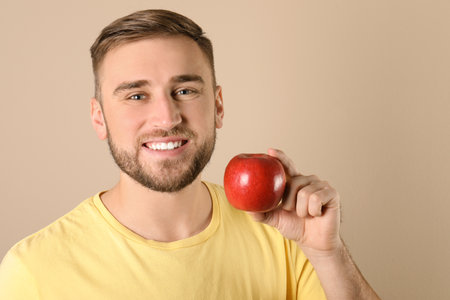 Young man with healthy teeth and apple on color background. Space for textの写真素材