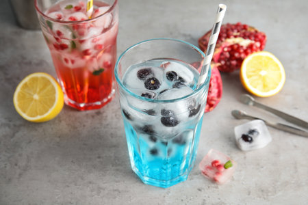 Tasty cocktails with fruit ice cubes on gray tableの写真素材
