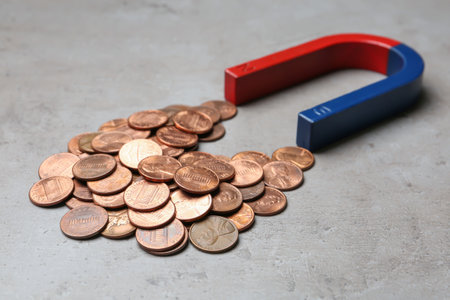 Magnet attracting coins on gray background, closeup. business concept