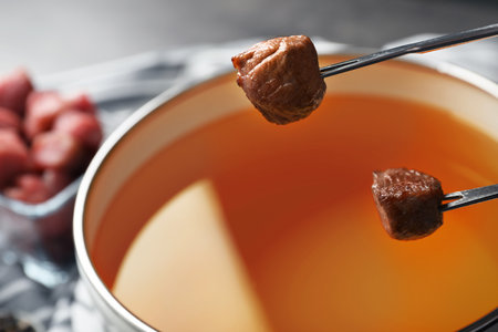 Dipping meat into fondue pot with oil on table, closeupの写真素材
