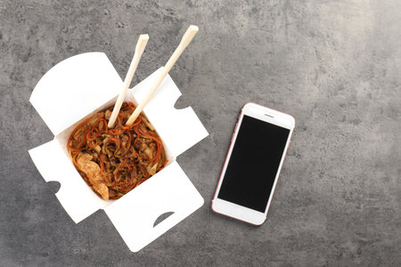 Smartphone with space for text and Chinese noodles on gray table, top view. food deliveryの写真素材