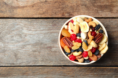 Bowl with different dried fruits and nuts on wooden background, top view. Space for textの写真素材