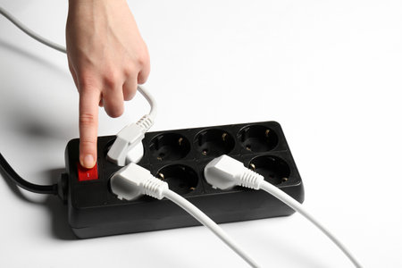Woman pressing power button of extension cord on white background, closeup. Electrician's equipment