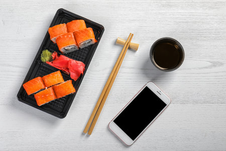 Flat lay composition with sushi rolls, smartphone and space for text on white wooden table. food deliveryの写真素材