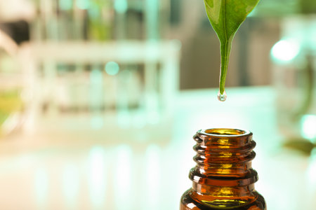 Clear drop falling from leaf into small bottle on blurred background, closeup with space for text. plant chemistryの写真素材