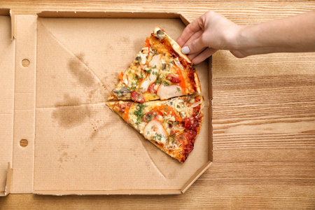 Woman taking pizza piece out of box on wooden table, top viewの写真素材